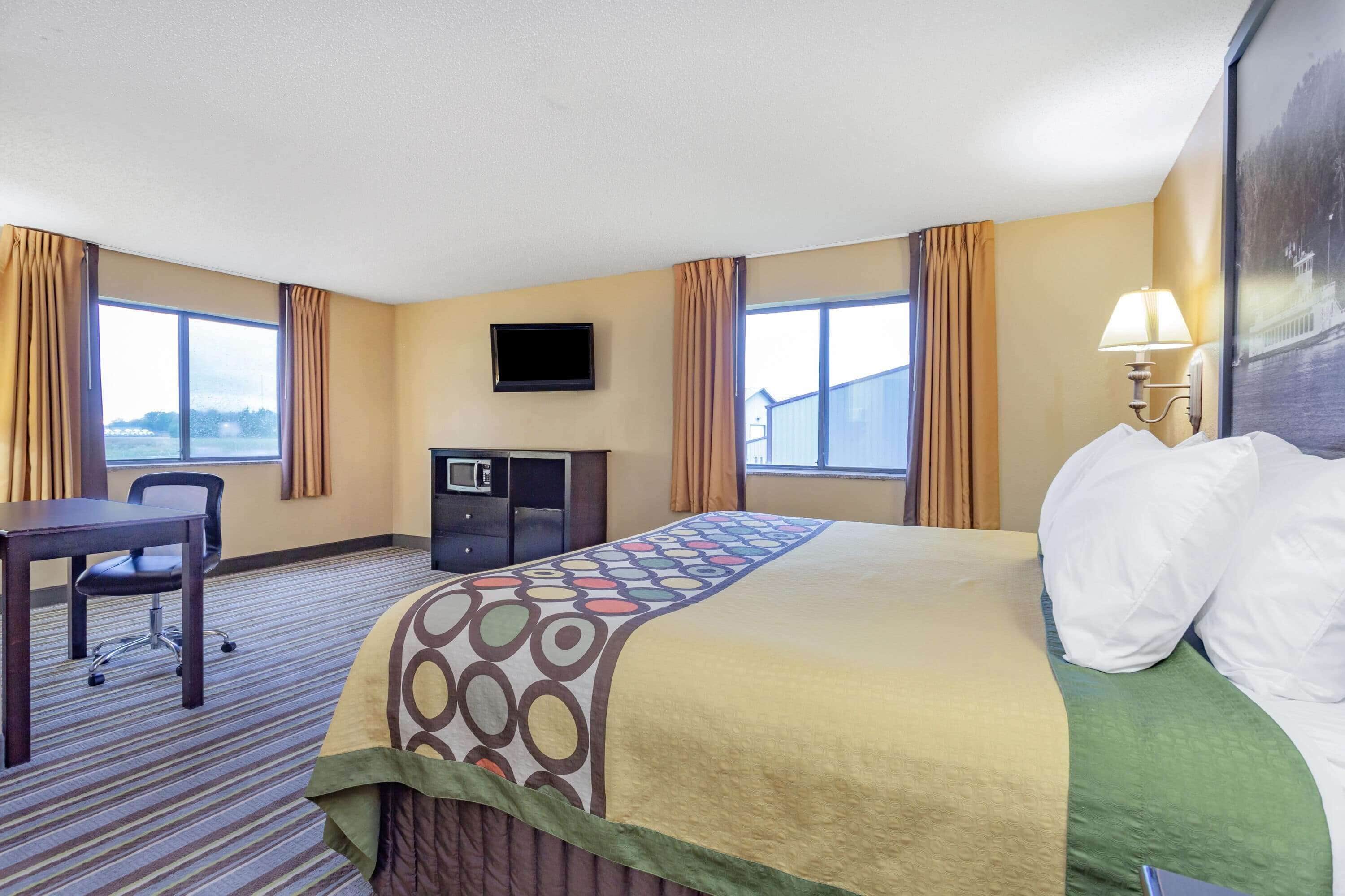 A hotel room with a large bed, a desk, a television, and a window with curtains.