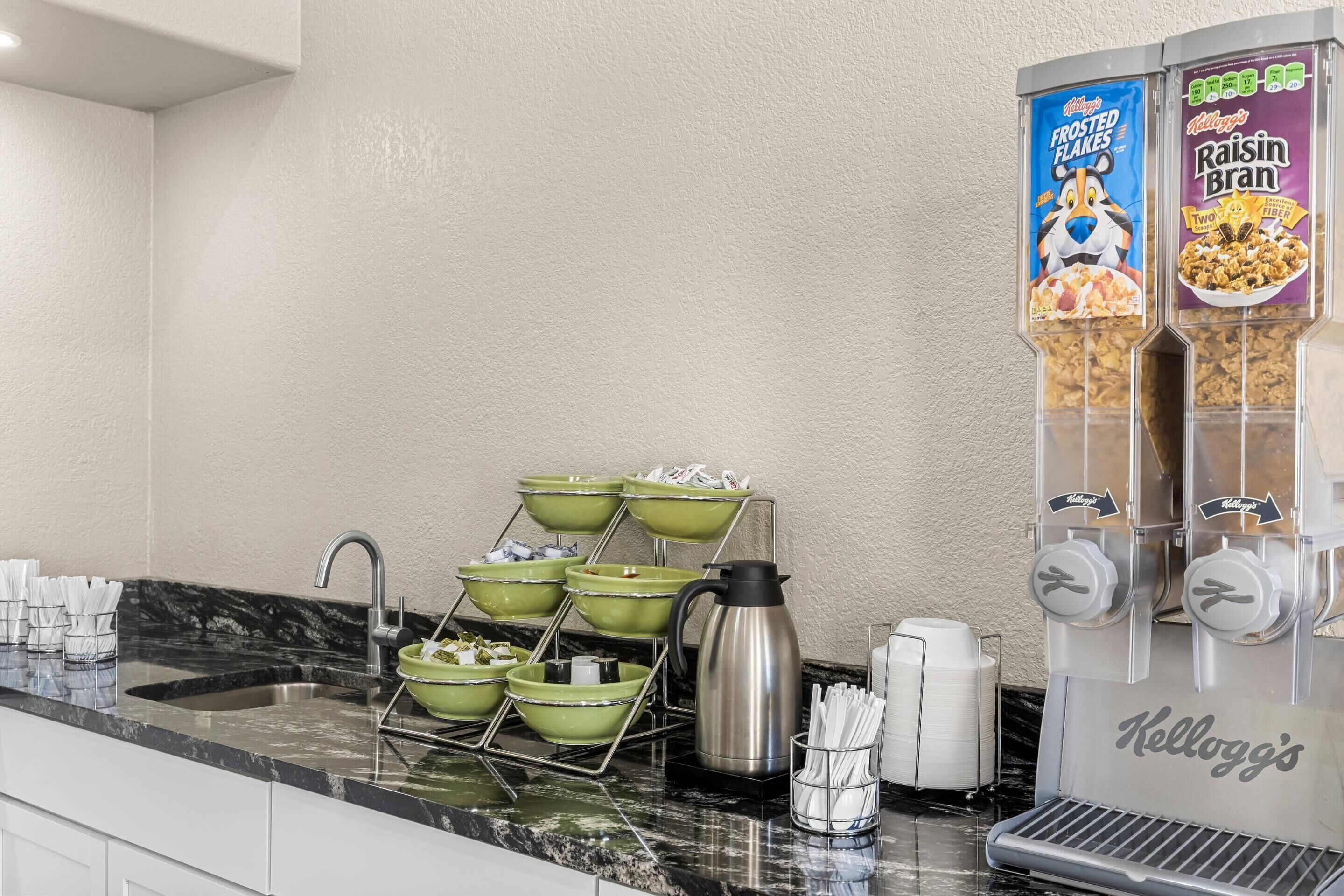 A kitchen with a marble countertop, a coffee maker, and a Kellogg's cereal dispenser.