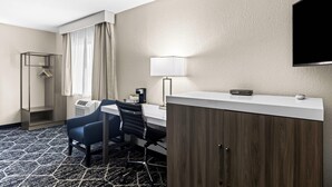Habitación de hotel con escritorio, silla, armario y televisión de pantalla plana montada en la pared.