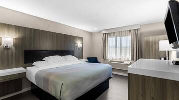 A hotel room with a bed, bedside tables, a desk, a chair, a TV, a window with curtains, and a wall-mounted air conditioning unit.