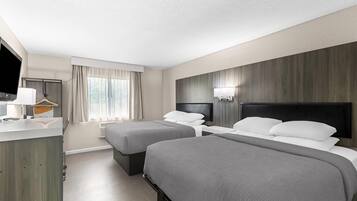 A hotel room with two beds, a desk, a chair, and a TV.