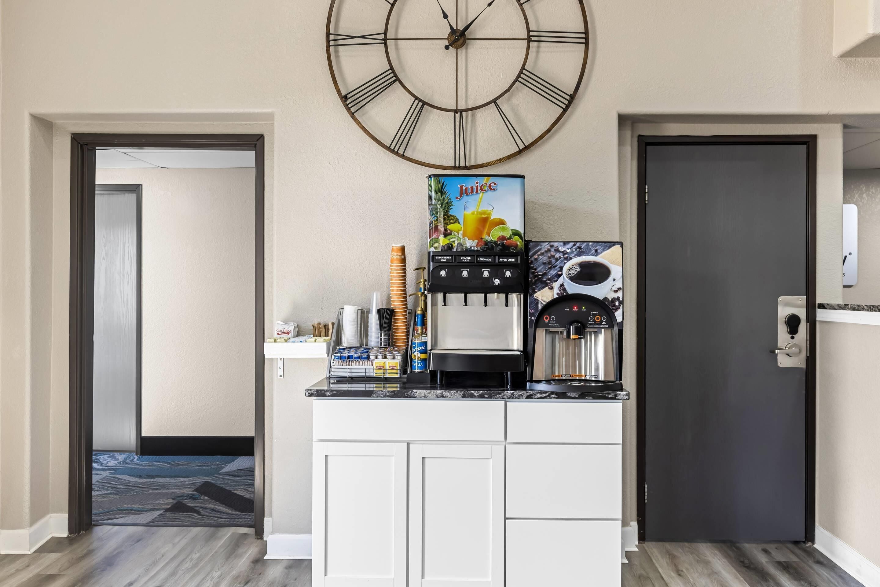 A kitchenette with a coffee machine, a juice dispenser, and a clock on the wall.