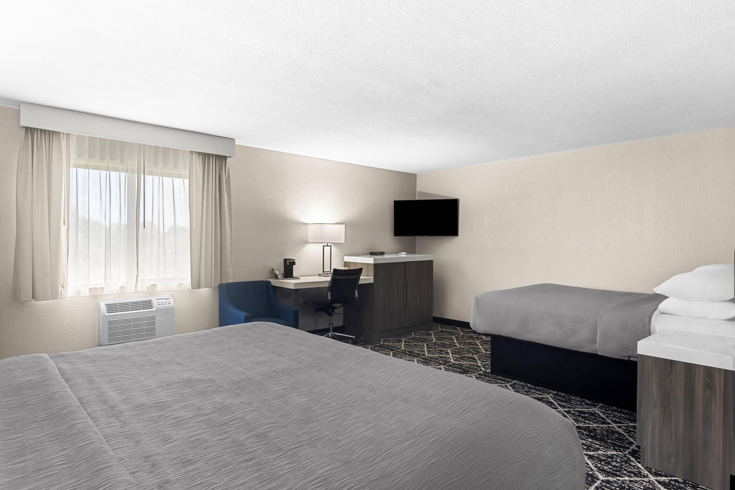A hotel room with a bed, desk, chair, TV, and a window with curtains.