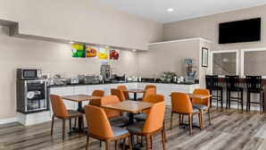 Cocina moderna con microondas, refrigerador y cafetera. Hay un comedor con sillas naranjas y una mesa.