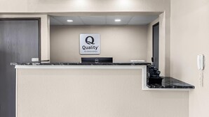 Un mostrador de recepción con un cartel que dice 'Quality by Choice Hotels', un teléfono y una encimera de mármol negro.