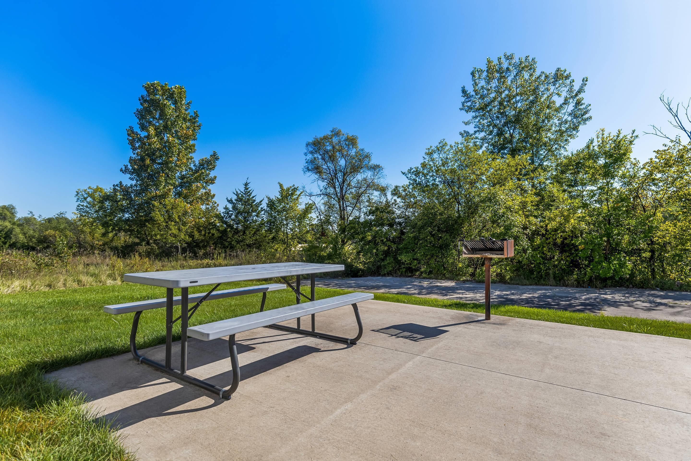A picnic table with benches, a signpost, and a paved area surrounded by grass and trees.