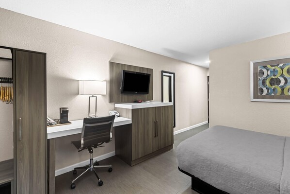 Habitación de hotel con cama, escritorio, silla, televisor y armario.