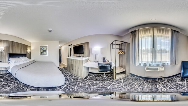 Una habitación de hotel moderna con una cama grande, un escritorio, una silla y un televisor.
