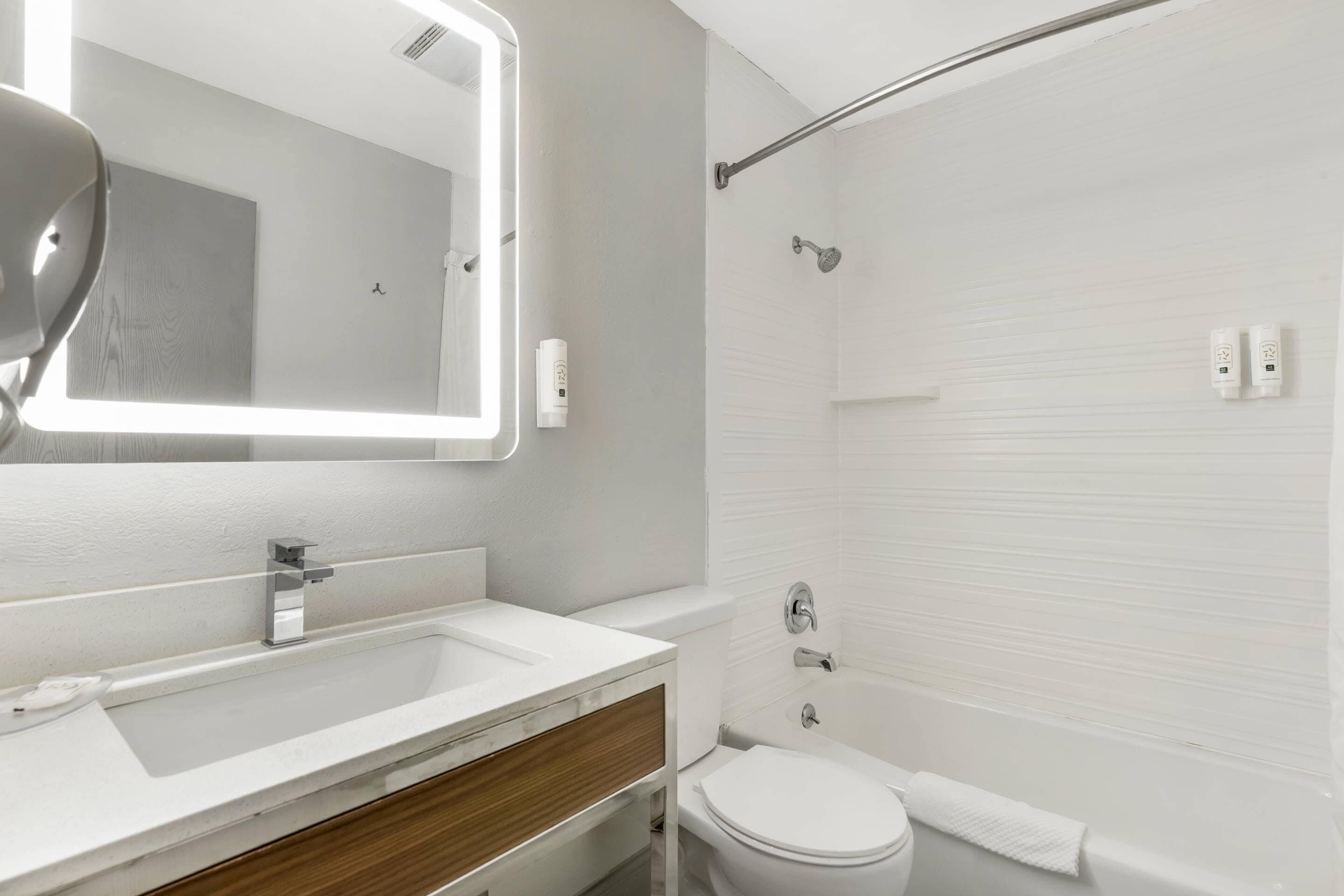 A modern bathroom with a white sink, mirror, toilet, and shower.