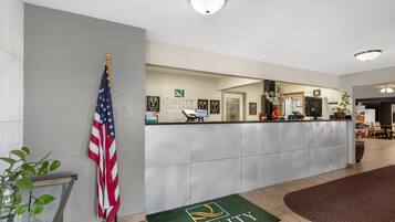 A hotel reception area with a reception desk, American flag, and a green doormat with the hotel logo.