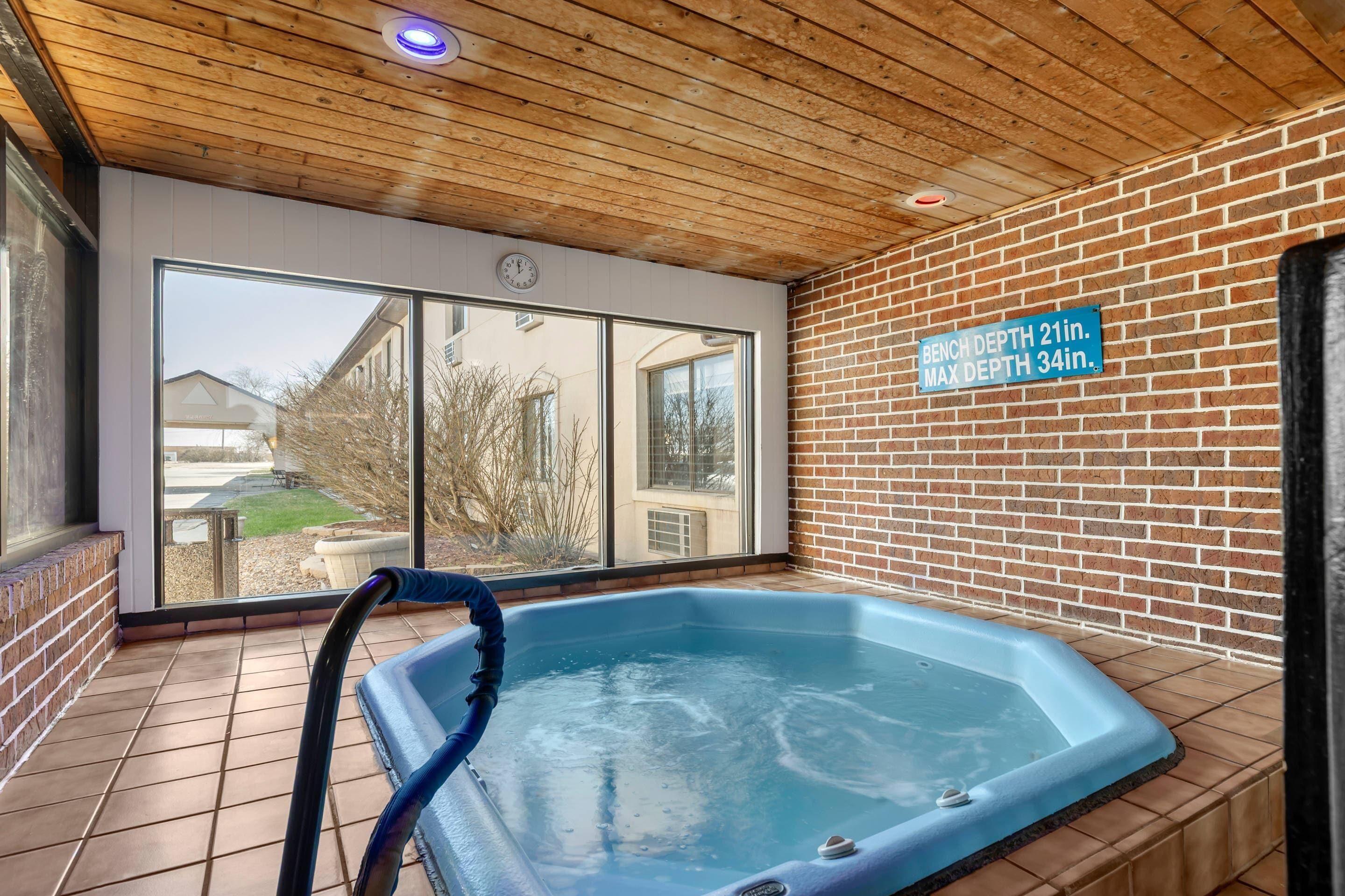 An indoor hot tub with a wooden ceiling and brick walls, large windows, and a sign indicating the tub's depth.