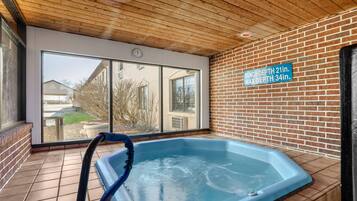 An indoor hot tub with a wooden ceiling and brick walls, large windows, and a sign indicating the tub's depth.