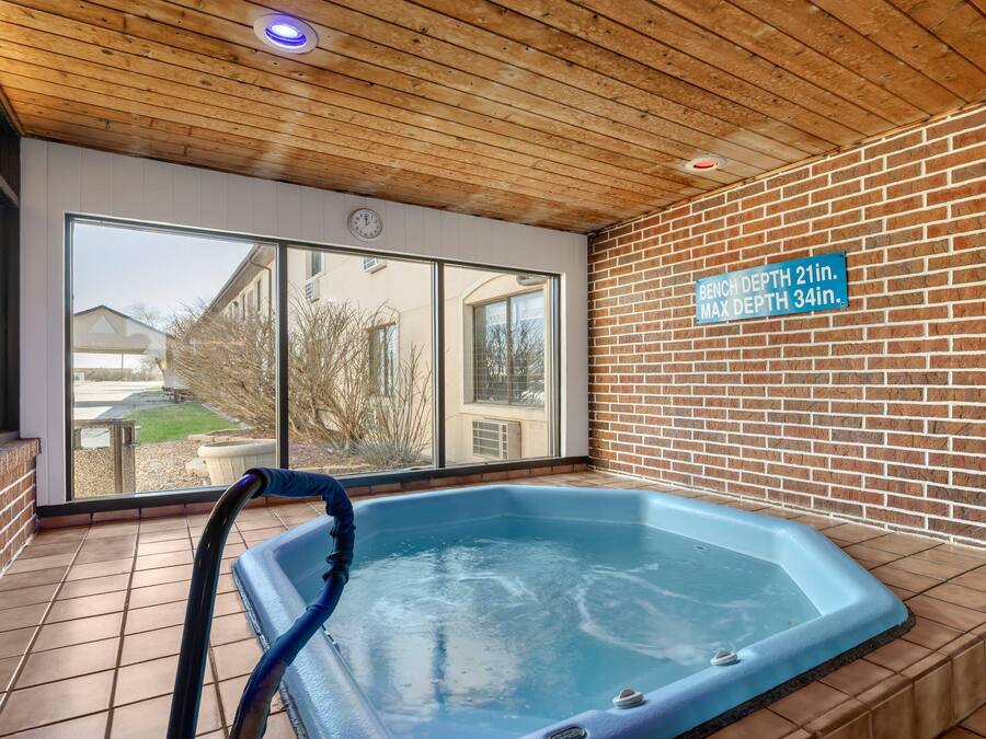 Jacuzzi interior amb sostre de fusta i parets de maó, finestrals amplis i un senyal que indica la profunditat de la banyera.