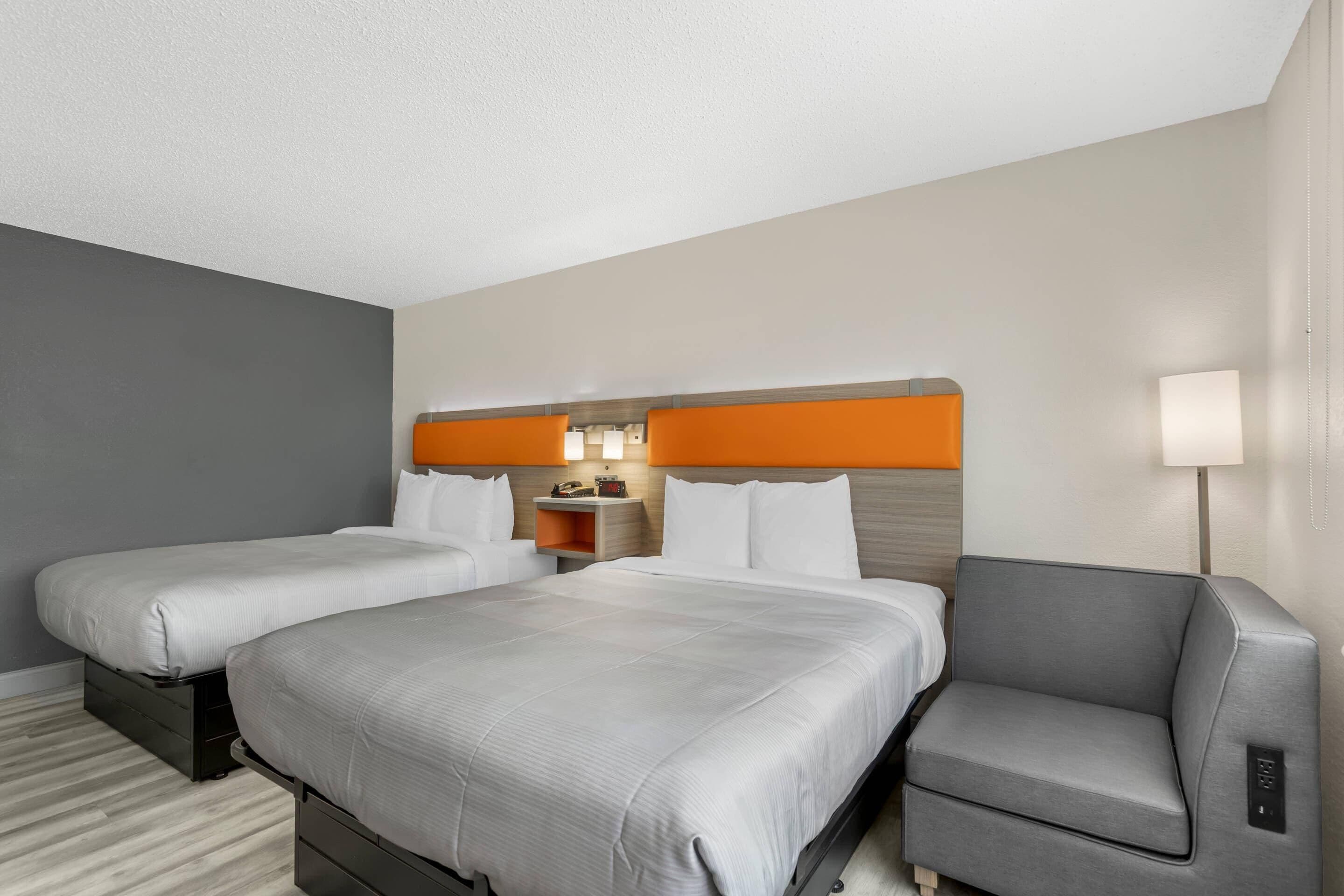 Ein Hotelzimmer mit zwei Betten, einem Schreibtisch, einem Stuhl und einem Nachttisch mit Lampe.