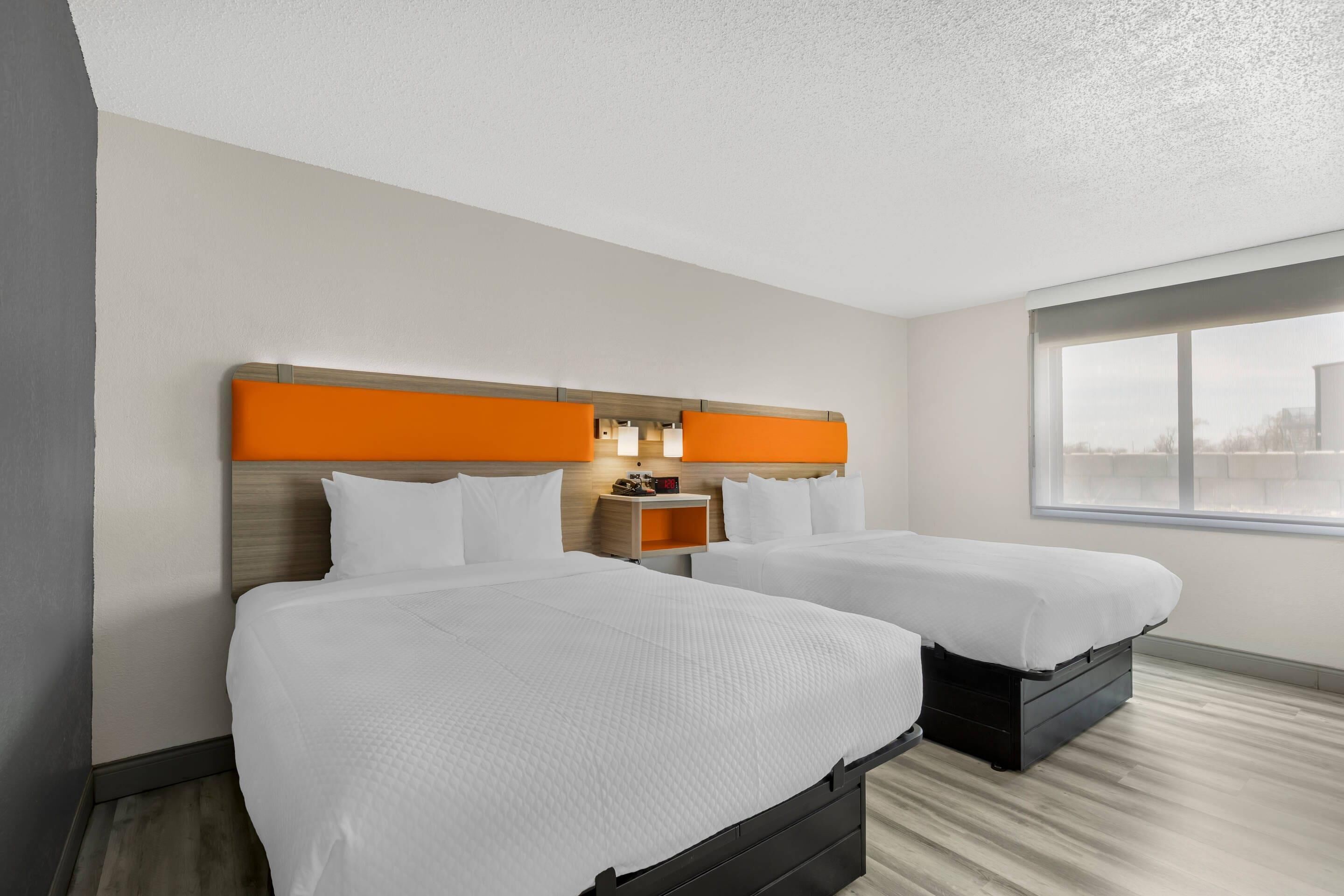 A hotel room with two beds, a wooden headboard, a nightstand, and a window.