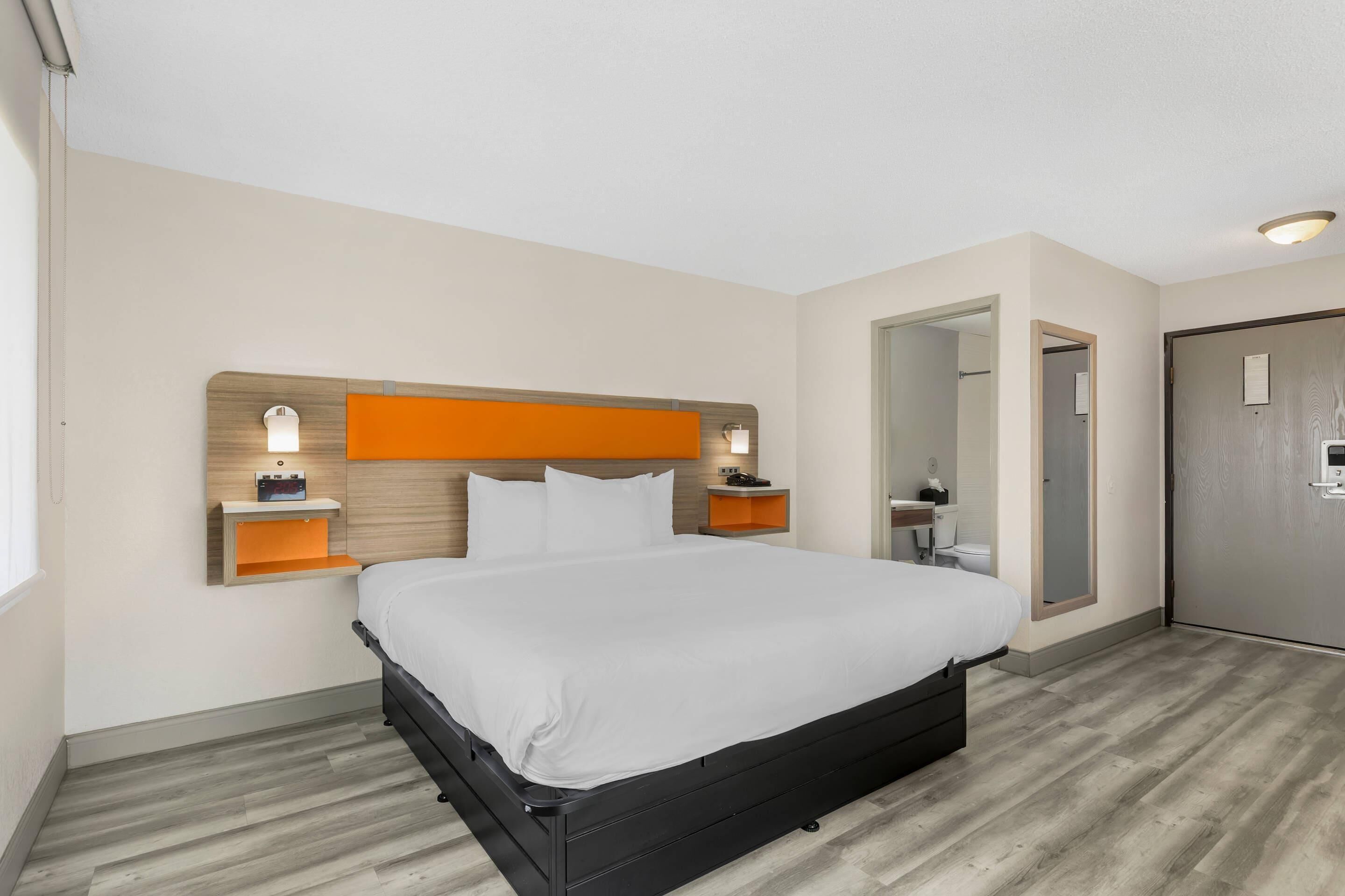 Une chambre d’hôtel avec un lit, deux tables de chevet, une commode, un miroir et une porte.