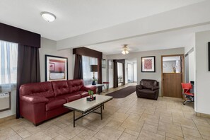 A spacious living room with a red leather sofa, a coffee table, a dark brown armchair, and a red office chair. - Quality Inn & Suites Ottumwa North (Ottumwa)