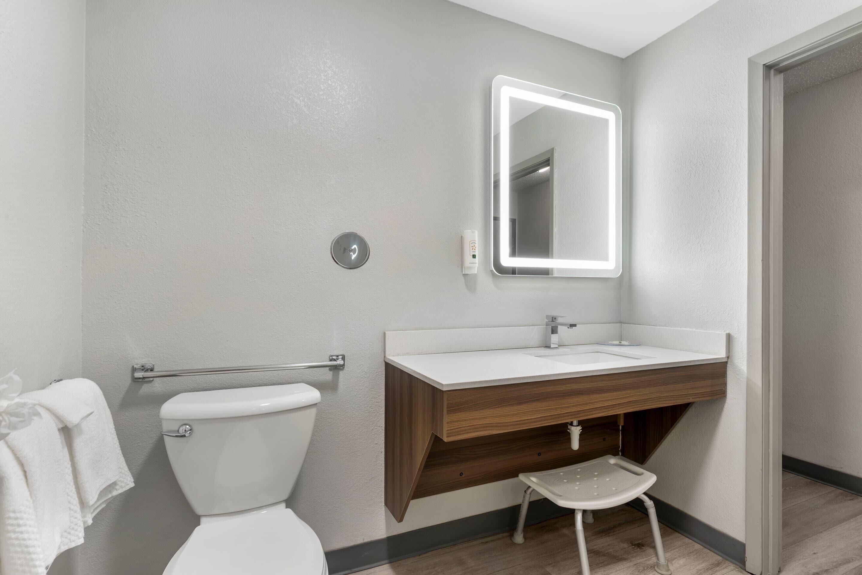 A bathroom with a toilet, a sink with a mirror, and a small stool.