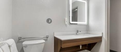 A bathroom with a toilet, a sink with a mirror, and a small stool.