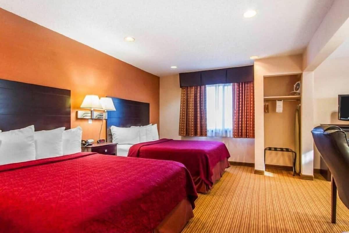 A hotel room with two beds, a desk, a chair, a TV, and a window with curtains.