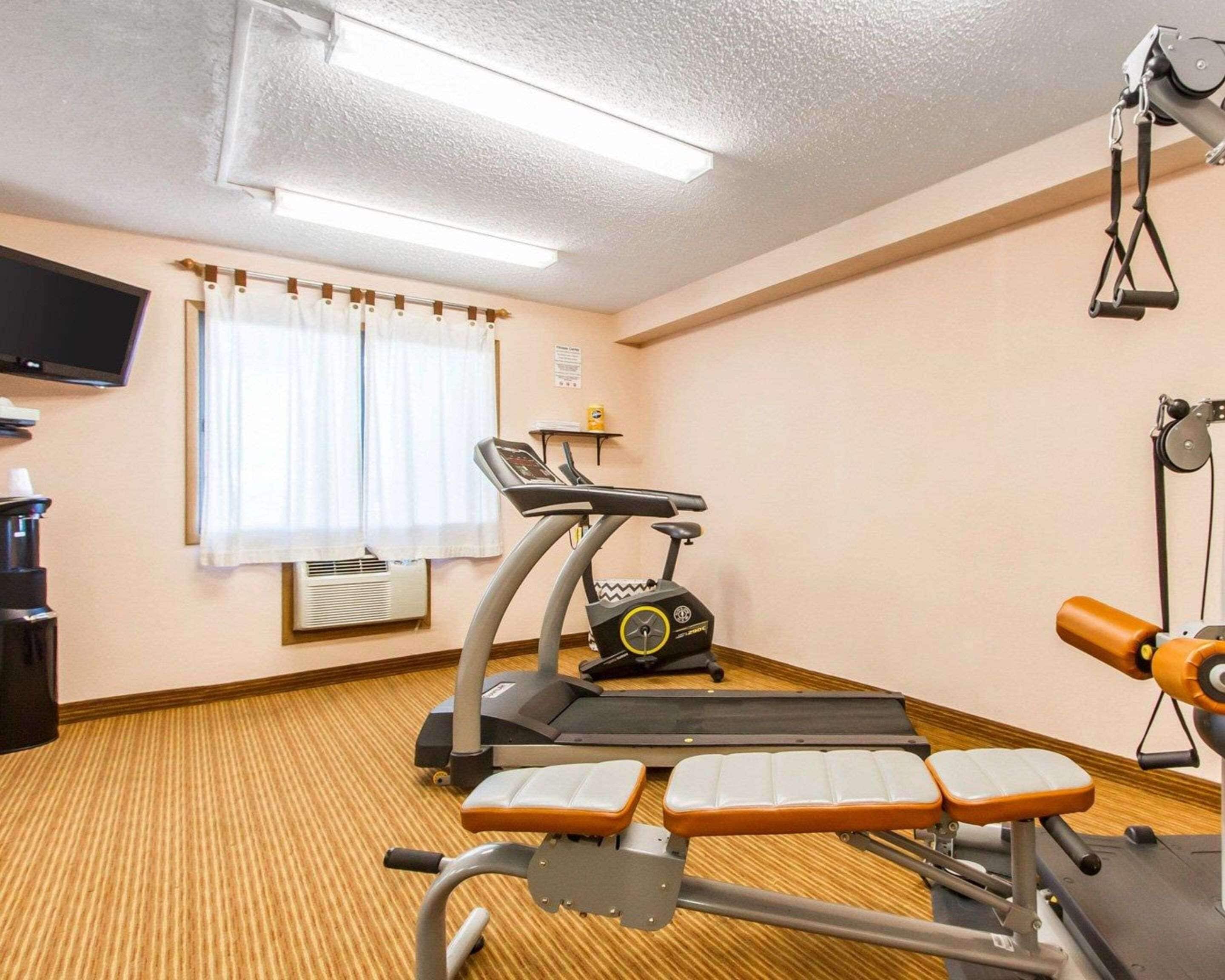 Habitación de hotel con una cinta de correr, banco de ejercicios y un televisor en la pared.