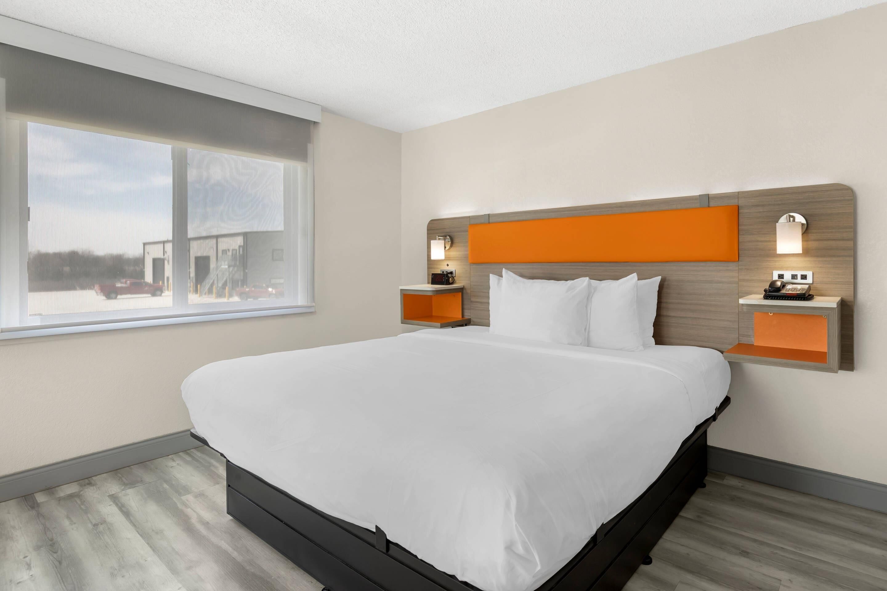 A modern hotel room with a large bed, a window with a view, and two bedside tables with lamps.