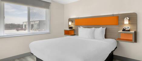 A modern hotel room with a large bed, a window with a view, and two bedside tables with lamps.