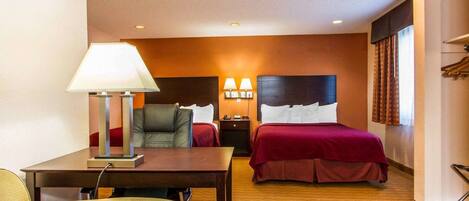 Habitación de hotel con cama, escritorio con lámpara, silla y mesita de noche.