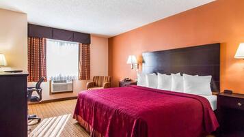 A hotel room with a large bed, a desk, a chair, and a window with curtains.