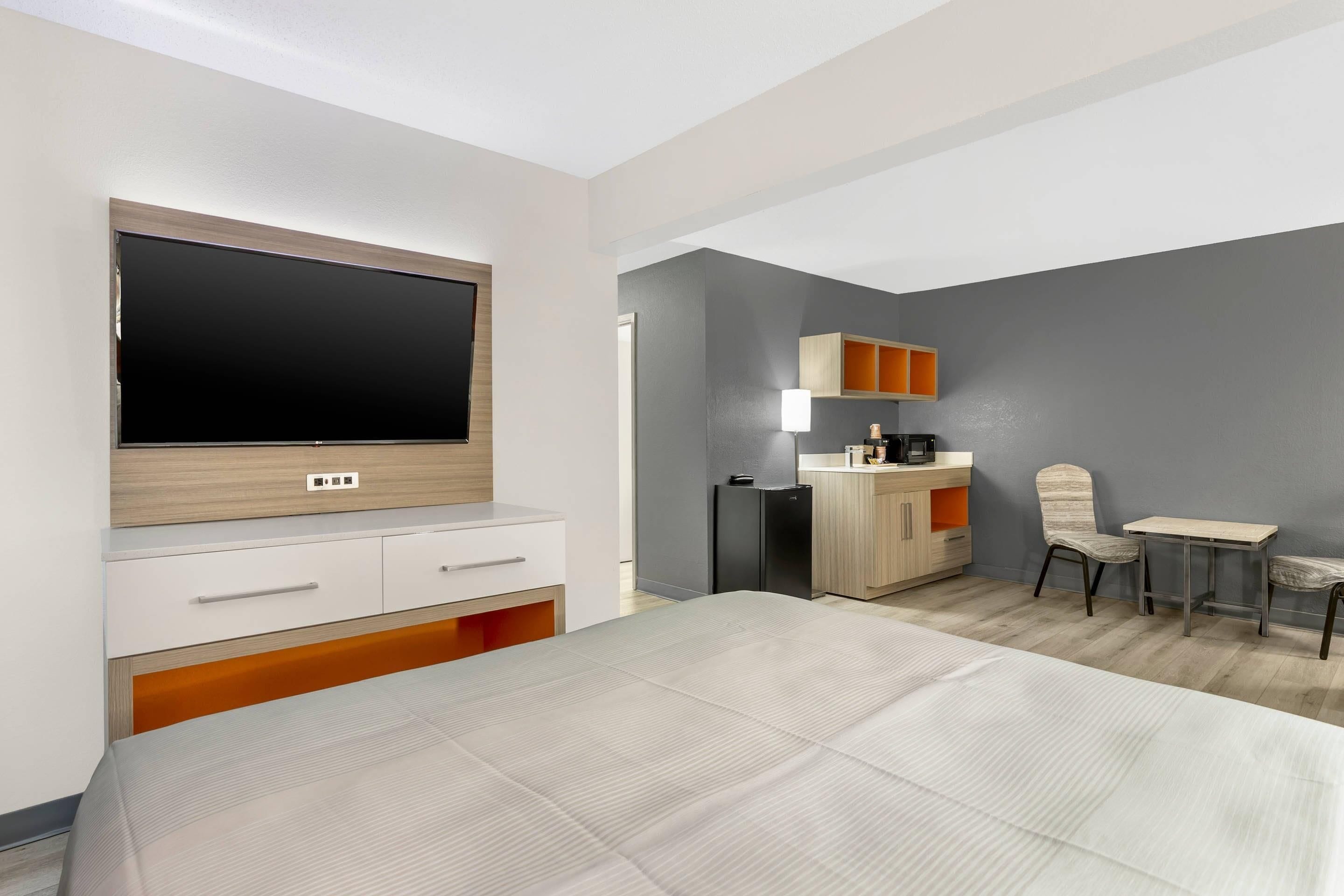A hotel room with a bed, a TV, a small kitchenette, and a seating area.