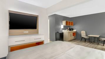 A hotel room with a bed, a TV, a small kitchenette, and a seating area.