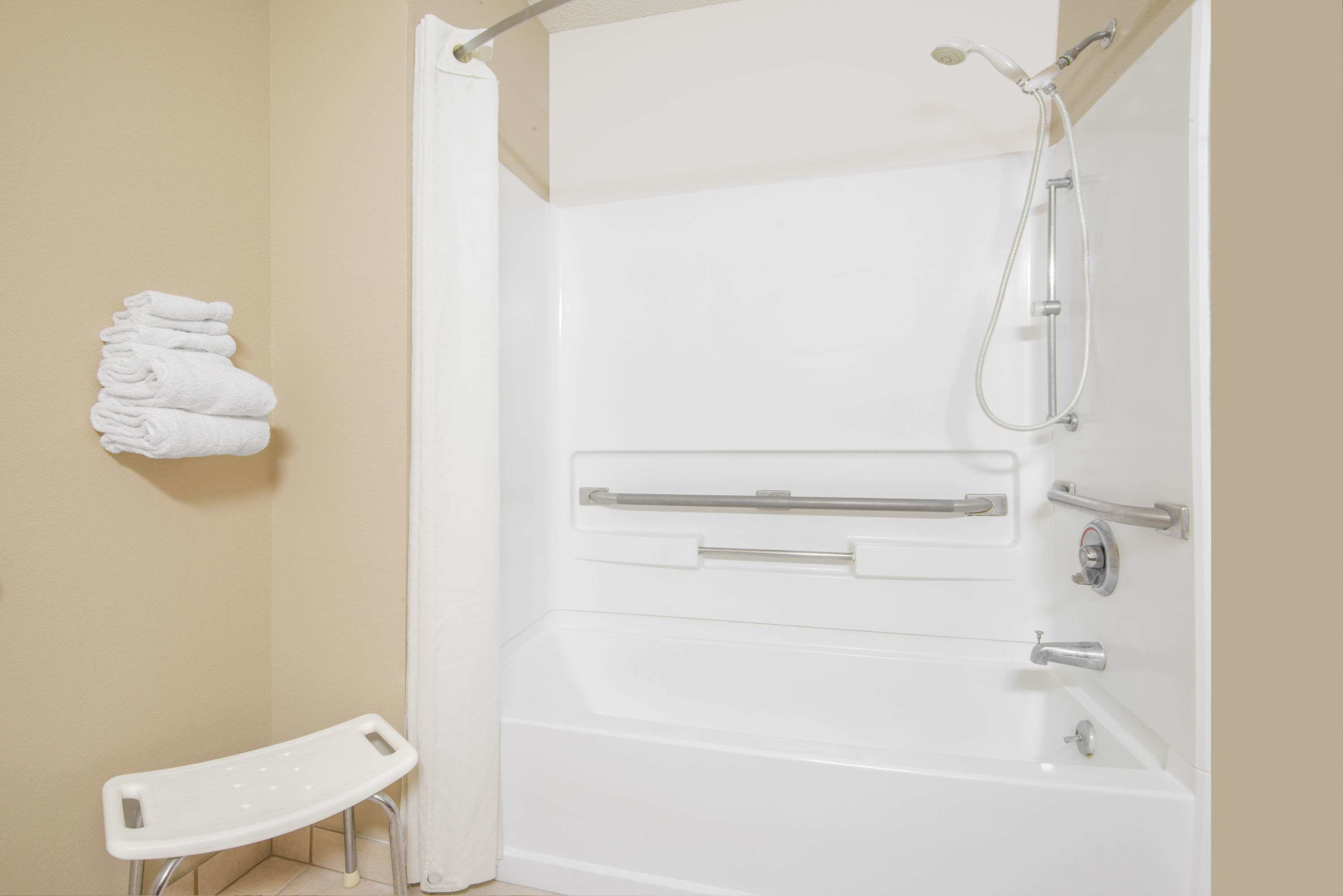 A white bathtub with a showerhead and grab bars, a white towel rack, and a white step stool.