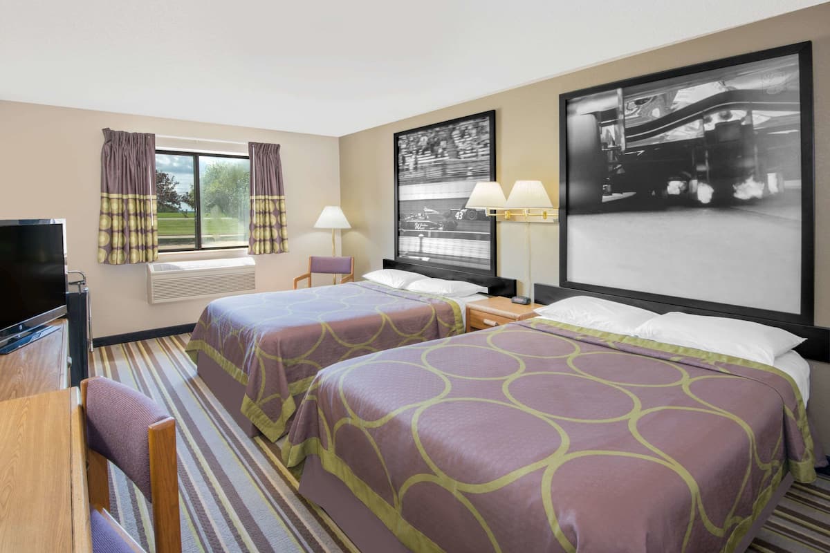 A hotel room with two beds, a desk, a chair, a television, and large windows with curtains.