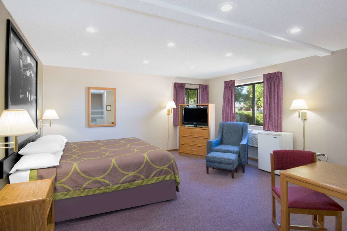 A hotel room with a bed, a desk, a chair, a television, a dresser, and a window with curtains.