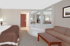 Una camera d'albergo con un letto, un divano, un tavolino, un bagno con vasca e uno specchio.