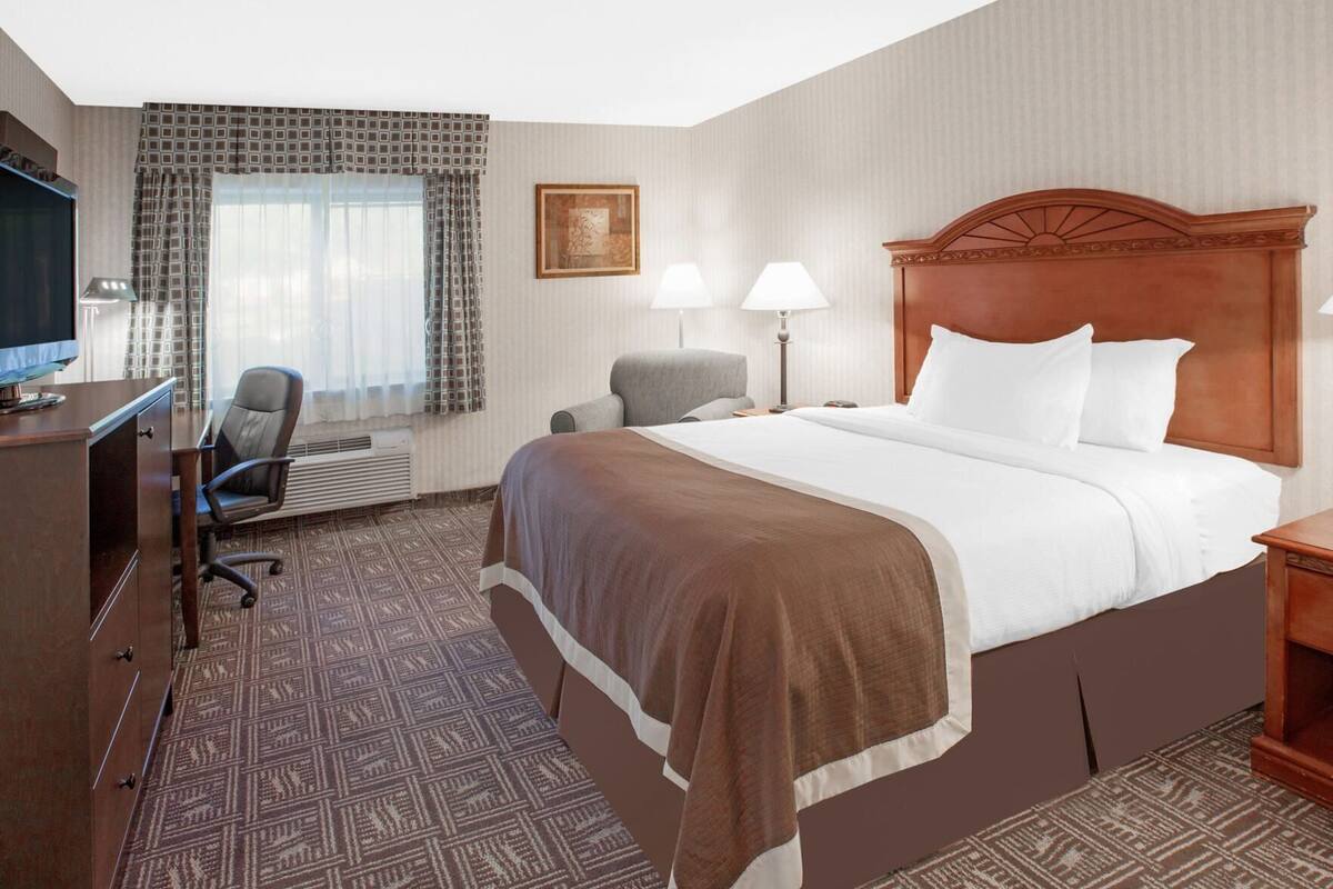 A hotel room with a bed, desk, chair, lamps, and a television.