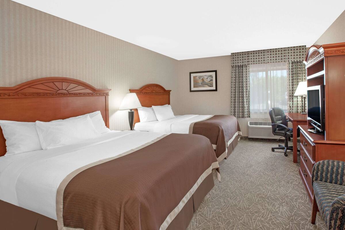 A hotel room with two beds, a desk, a chair, a television, and an air conditioning unit.