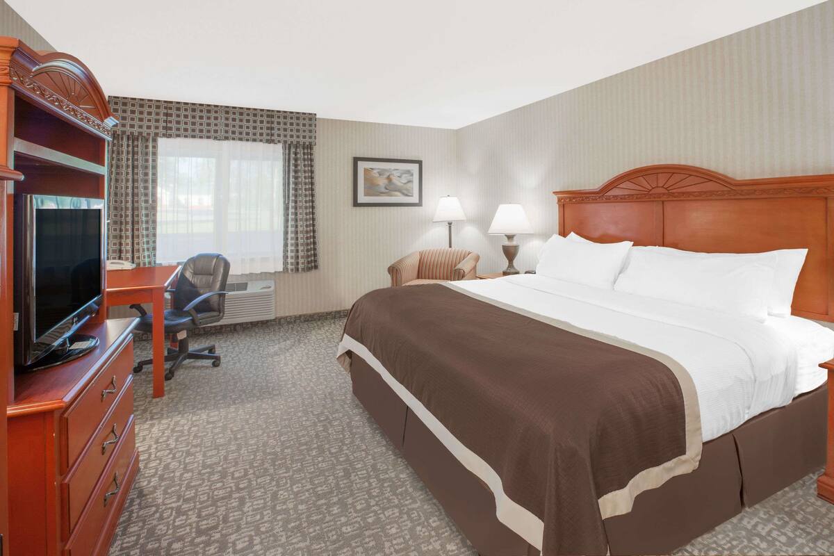A hotel room with a large bed, a desk with a television, a chair, and two bedside lamps.