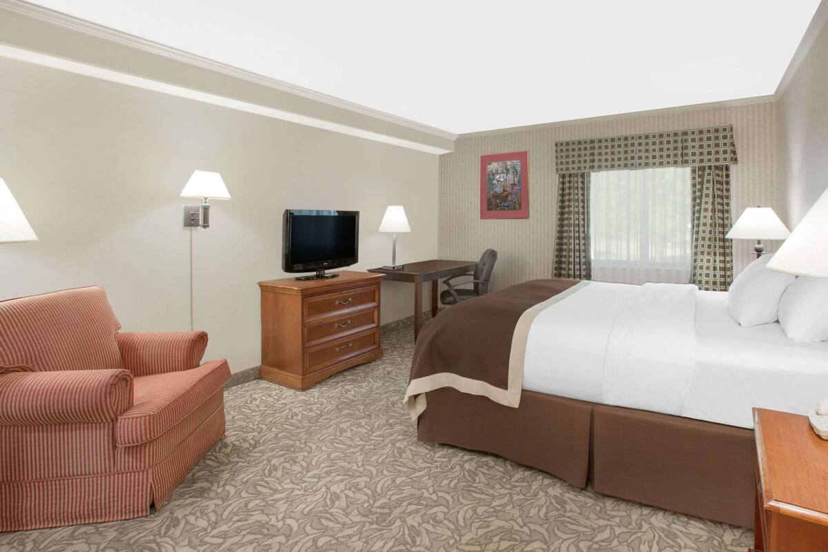 A hotel room with a bed, a desk, a television, a chair, and a lamp.