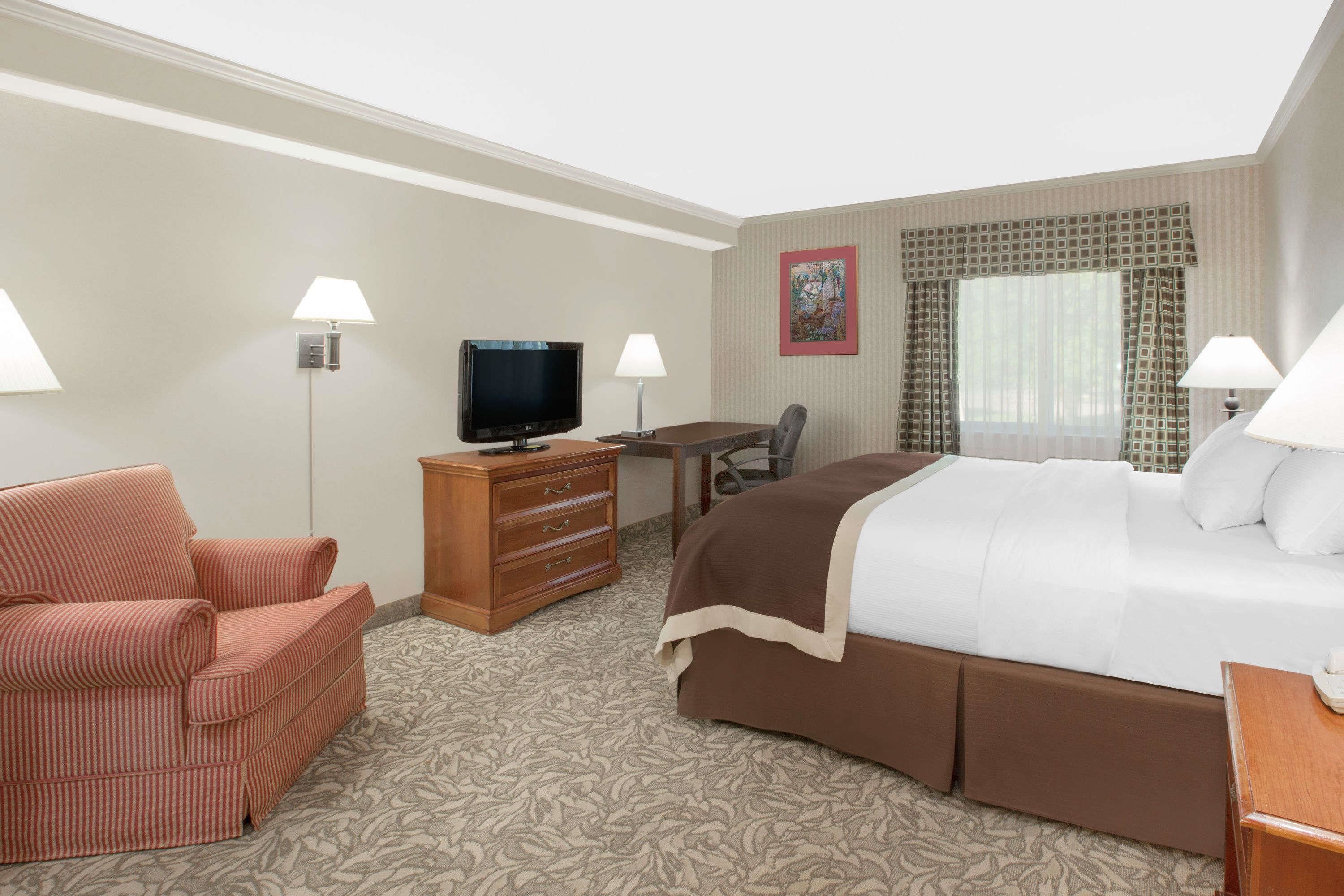 A hotel room with a bed, a desk, a television, a chair, and a lamp.