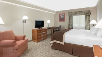 A hotel room with a bed, a desk, a television, a chair, and a lamp.