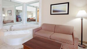 A hotel room with a large bathtub, a sofa, a coffee table, a floor lamp, and a framed picture on the wall. - Baymont by Wyndham Jackson (Jackson)