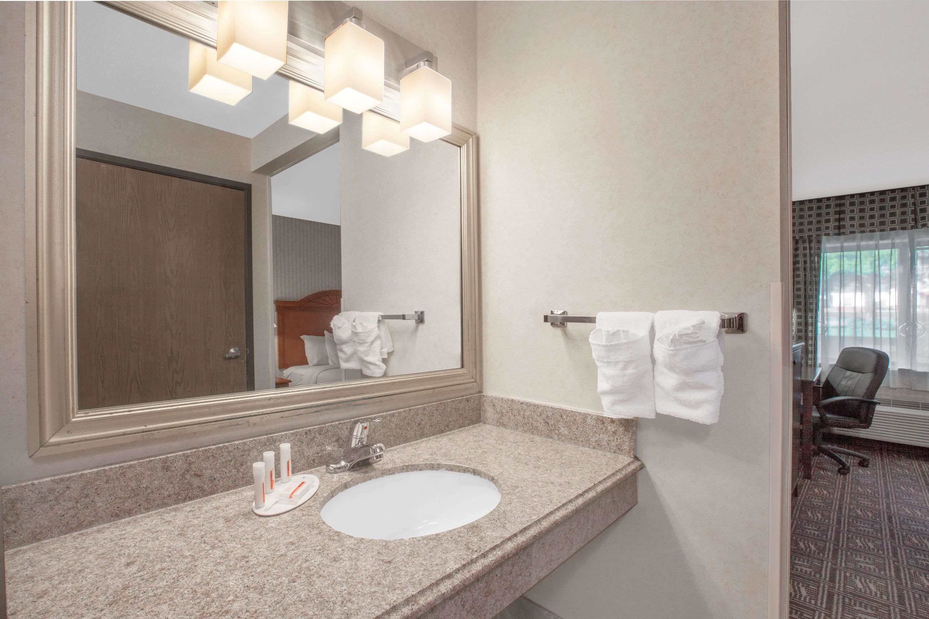 A bathroom with a granite countertop, a white sink, a large mirror, and a towel rack with white towels.