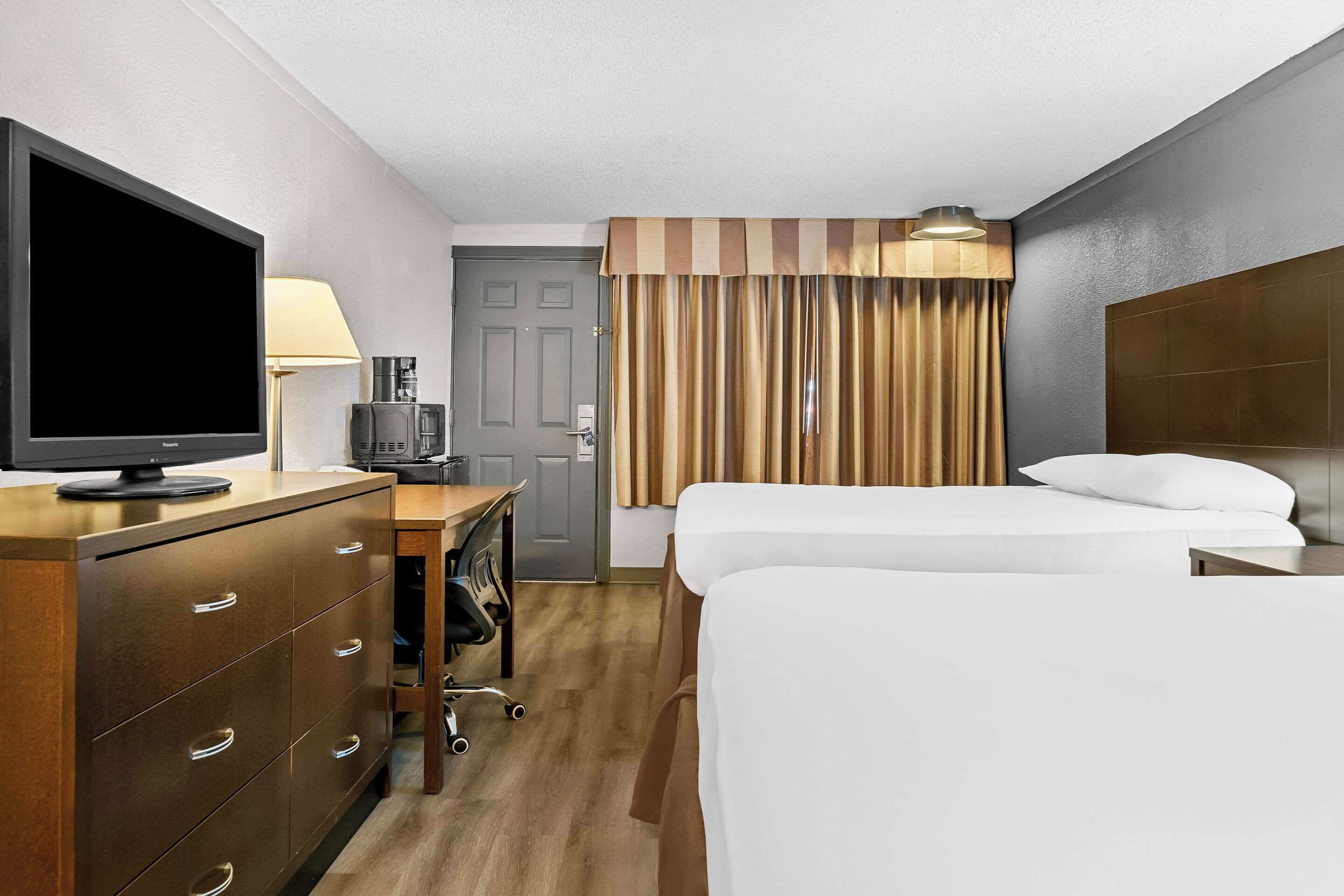 Una habitación de hotel con dos camas, televisor, escritorio con lámpara y cafetera.