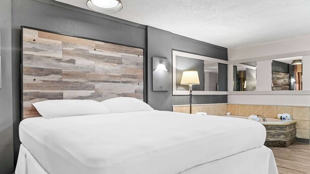 Een hotelkamer met een groot bed, een houten hoofdeinde, een nachtkastje met lamp, een spiegel en een klein badgedeelte.