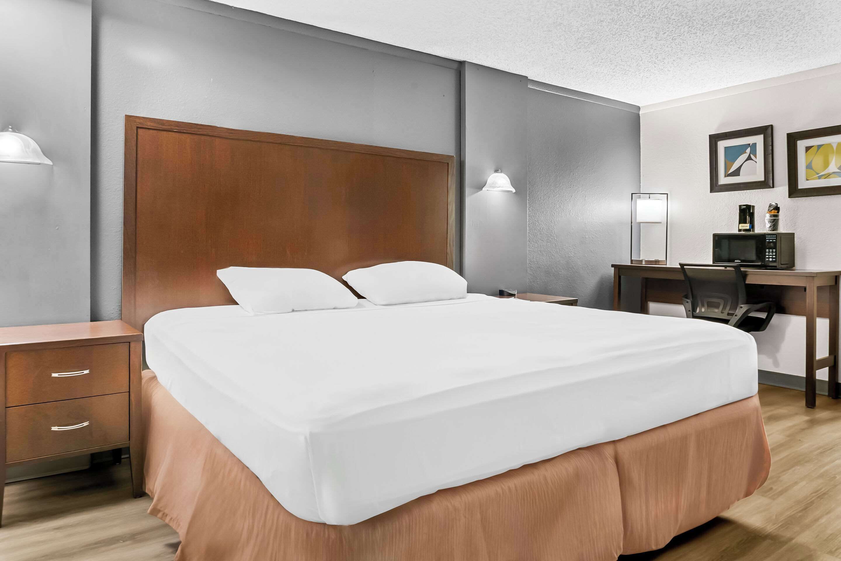Habitació d'hotel amb un llit gran, una taula de treball amb un ordinador, una cadira i una nitzeta amb calaixos.