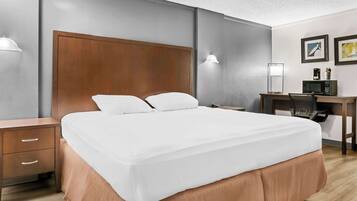 Habitació d'hotel amb un llit gran, una taula de treball amb un ordinador, una cadira i una nitzeta amb calaixos.
