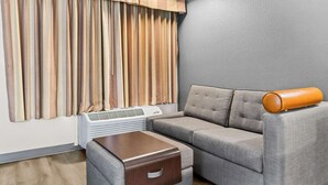 Een moderne woonkamer met een grijze bank, een houten bijzettafeltje en een witte airconditioner.