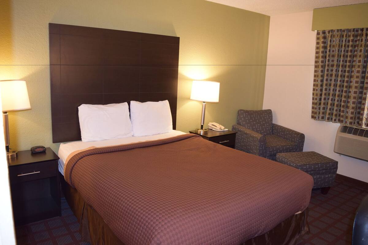 Una habitación de hotel con una cama grande, dos lámparas de noche, una silla, una mesita de noche y un teléfono.