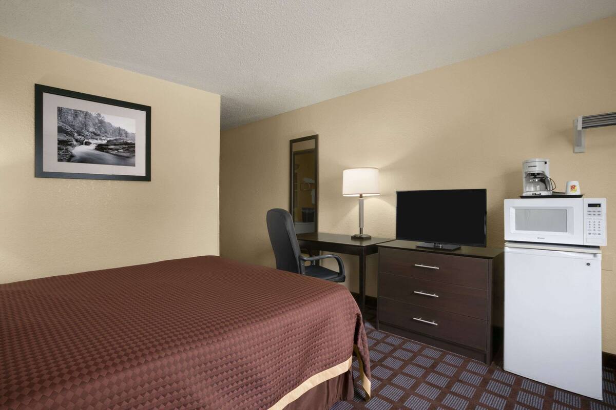 Una habitación de hotel con una cama, un escritorio con televisor, un microondas y un refrigerador.